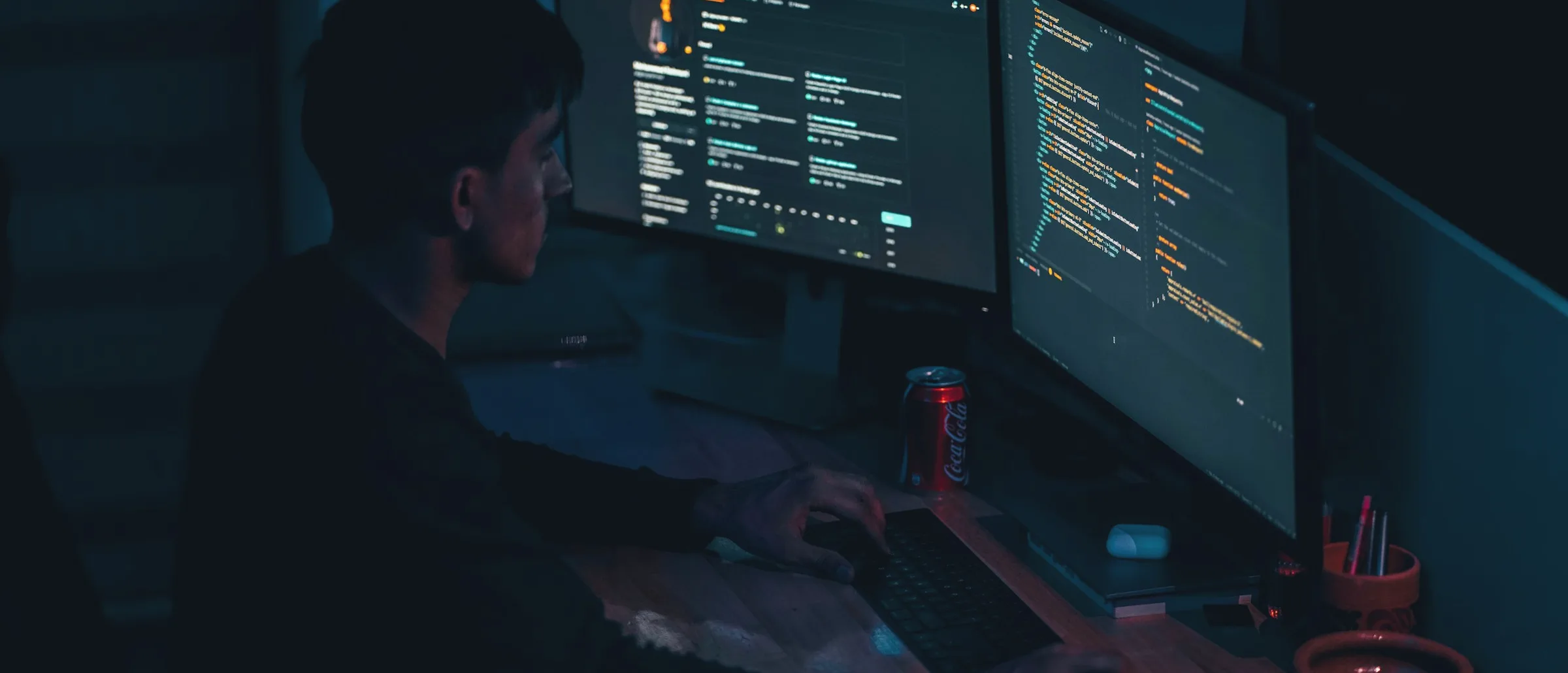 An engineer's desk in the Dehradun office, code on both monitors and foothill light through the window.